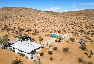 Aerial view of a desert home in Joshua Tree, featuring a swimming pool, outdoor seating area, and surrounding arid landscape.