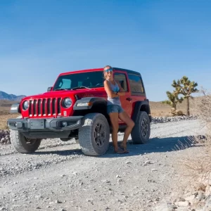 Ali from She Explores the USA, leaning against a red Jeep with a Joshua Tree in the background