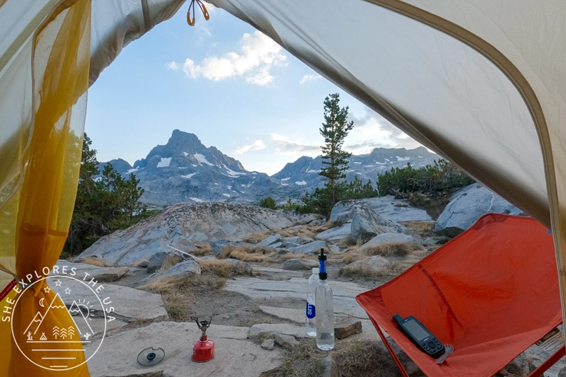Adventure Travel Insurance for Hikers & Backpackers - mountain views from inside a tent with backpacking supplies and a garmin inreach in the foreground