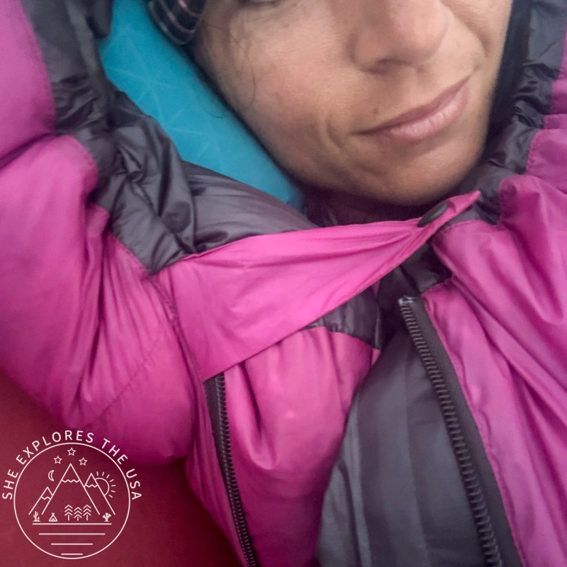 A woman zipped inside a Feathered Friends Petrel 10 UL sleeping bag with the neck draft collar fastener secured around her neck.