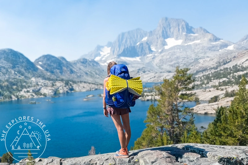 Woman hiking at Garnet Lake with blue backpack and sleeping pad on rocky Sierra Nevada trail - My Complete Outdoor Gear List (Updated 2026)