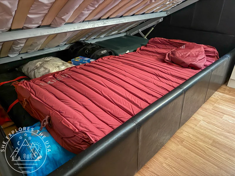 Exped MegaMat Max sleeping pad seen with the valves open underneath a lifted bed frame for long term storage.