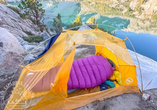 Feathered Friends Petrel UL 10 sleeping bag inside a tent overlooking an alpine lake during a backcountry camping trip.