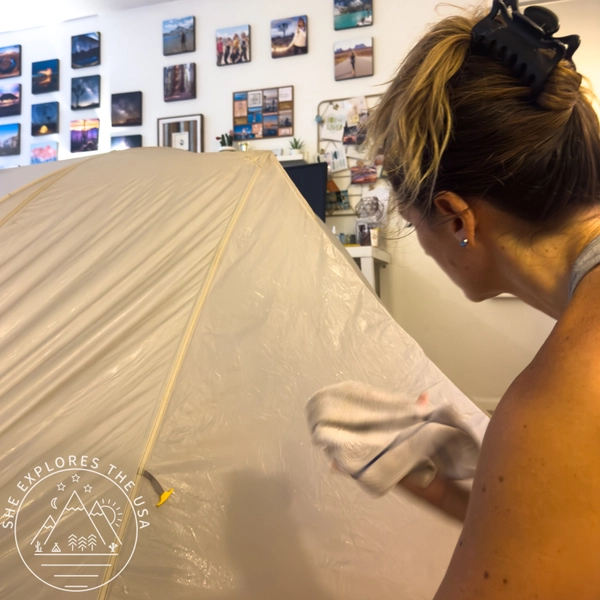 Working section by section with a cloth to clean and treat an aging tent rainfly indoors